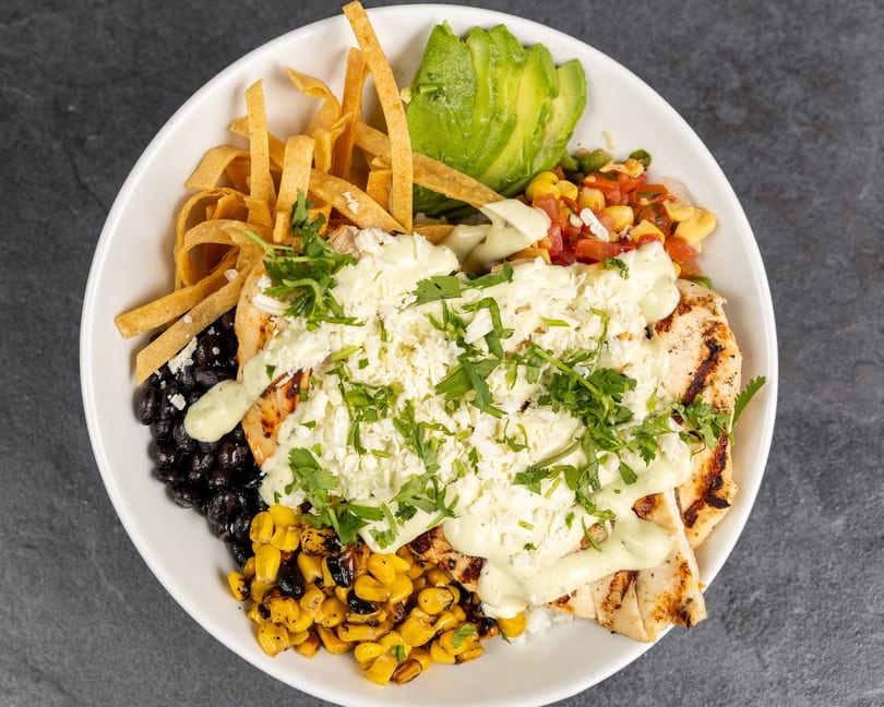 Grilled chicken bowl with black beans, corn, avocado, tortilla strips, cheese, and cilantro.