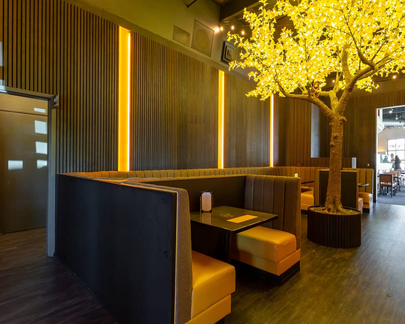 Restaurant interior with dark wood paneling, orange booth seating, and a large illuminated tree.
