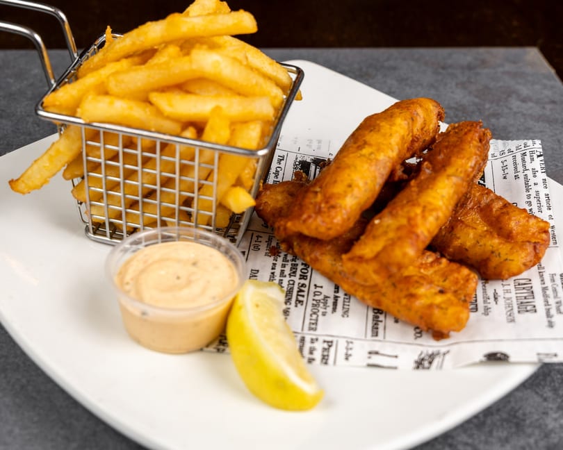 Crispy fish and chips served in a metal basket with a lemon wedge and dipping sauce.