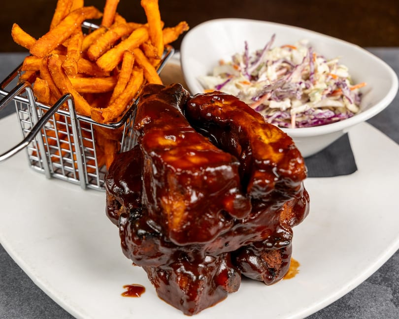 BBQ ribs with sweet potato fries in a metal basket and a side of coleslaw.