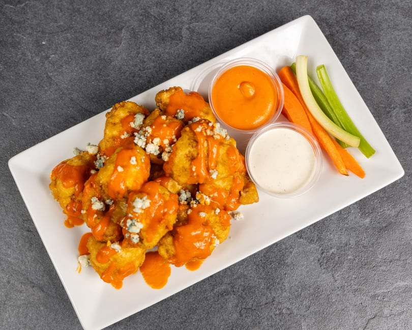 Buffalo cauliflower bites with blue cheese crumbles, buffalo sauce, ranch, carrots, and celery.