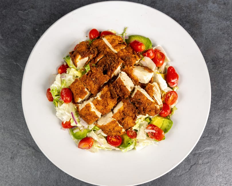 Crispy chicken salad with cherry tomatoes, avocado, and red onion on a white plate.