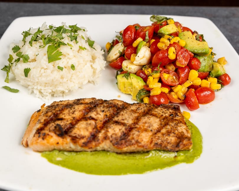 Grilled salmon on green sauce with white rice and a tomato, corn, avocado salad.