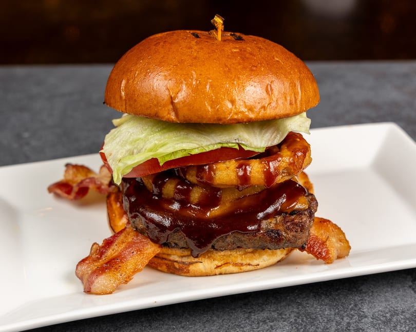A BBQ bacon cheeseburger with lettuce, tomato, and onion rings on a white plate.
