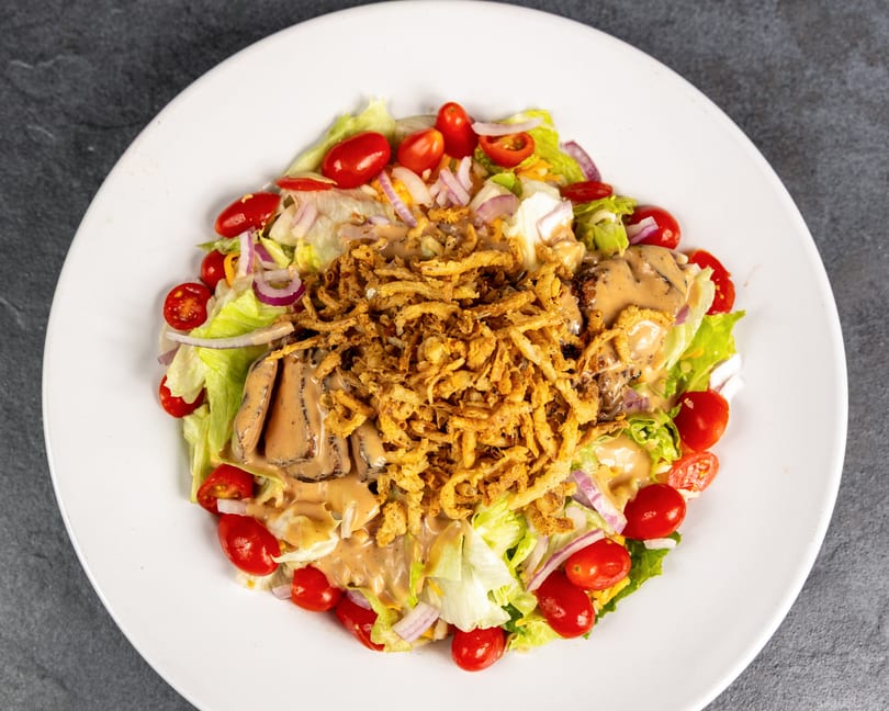 Steak salad with cherry tomatoes, red onions, crispy fried onions, and creamy dressing.